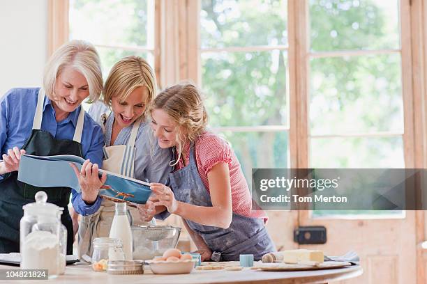 multi-génération de femmes à la recherche d'un livre de cuisine et pâtisserie de kitch - traditional home magazine photos et images de collection