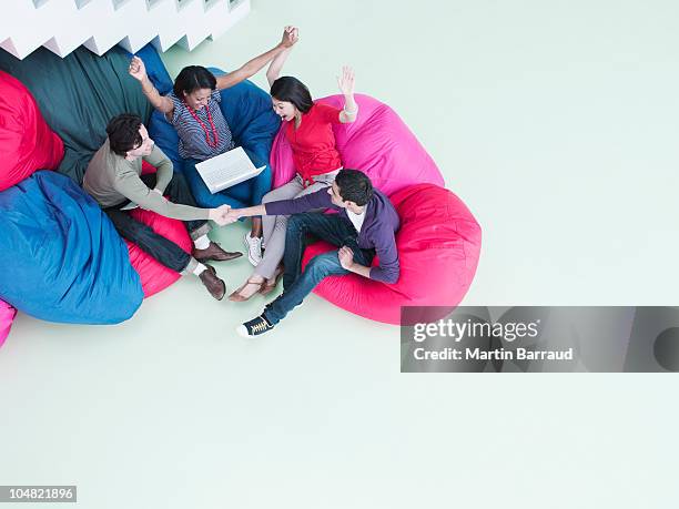 excited business people with arms raised sitting in bean bag chairs and looking at laptop - handshake isolated stock pictures, royalty-free photos & images