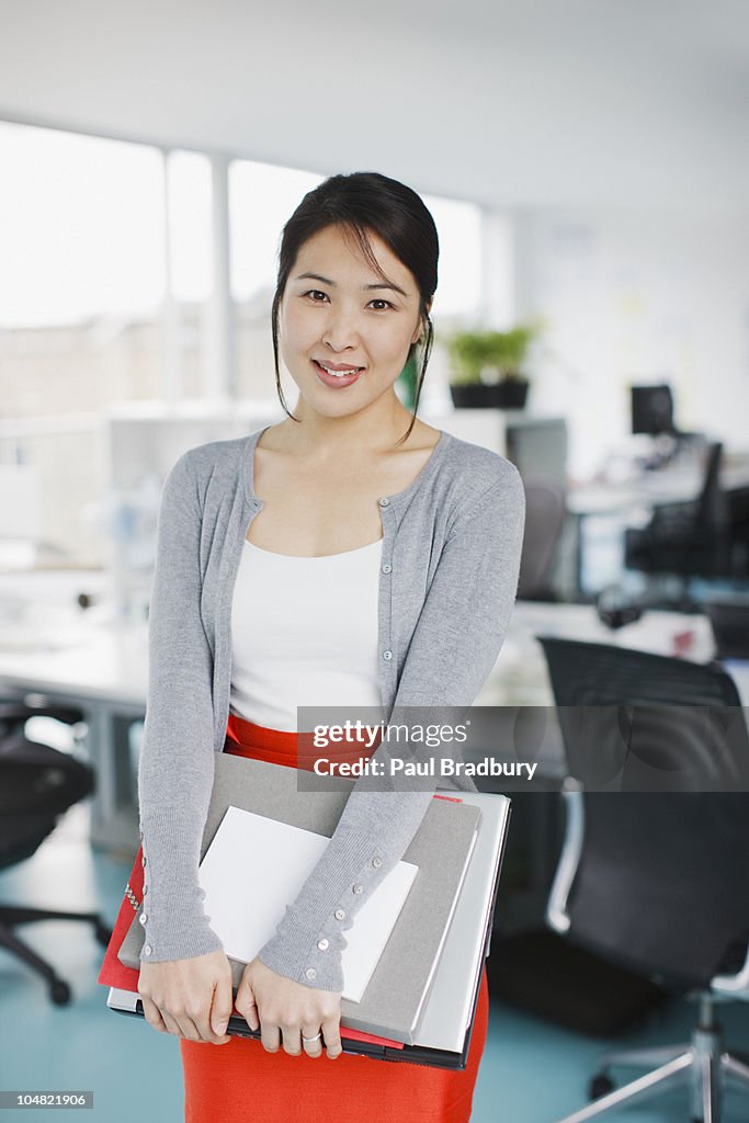 Smiling businesswoman holding laptop and folders in office