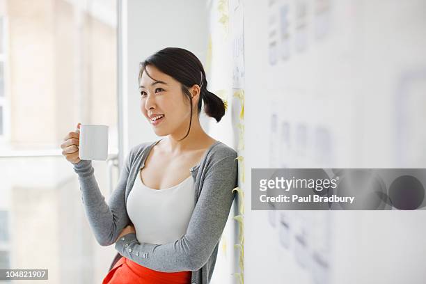 smiling businesswoman leaning against whiteboard and drinking coffee - coffee drink stock pictures, royalty-free photos & images