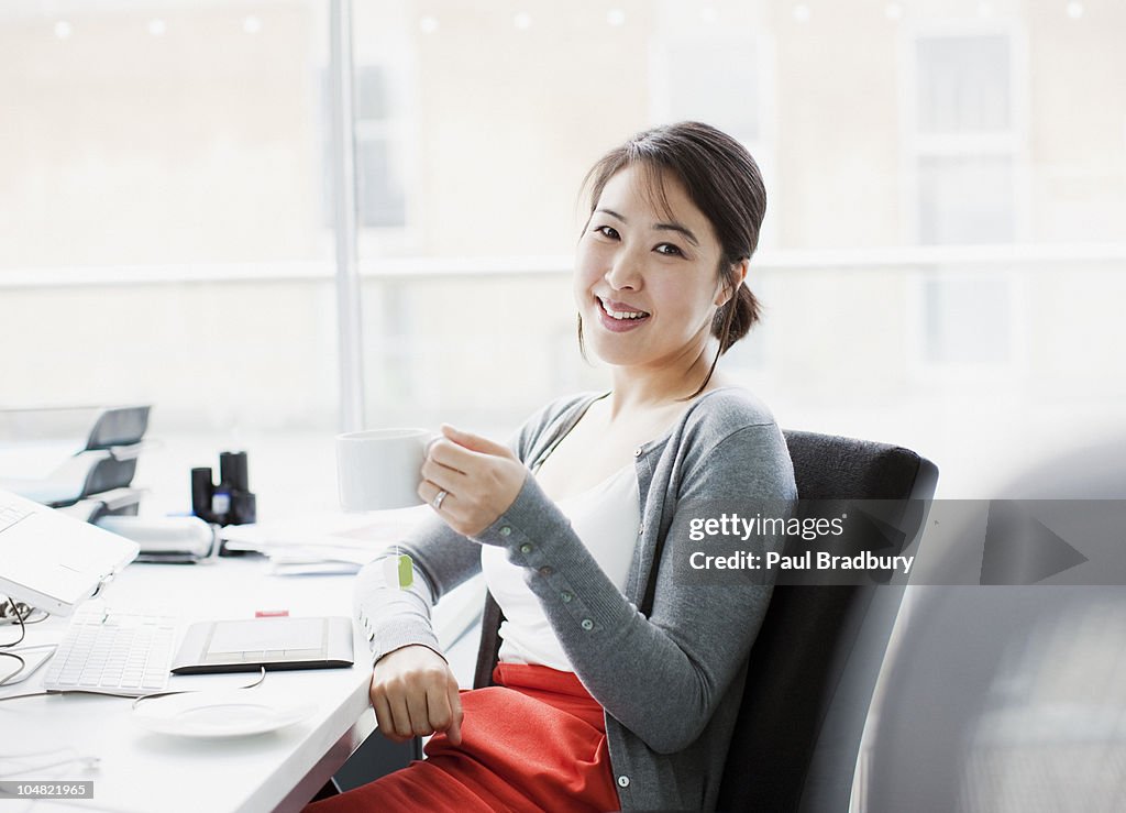 Smiling businesswoman drinking coffee at desk in office