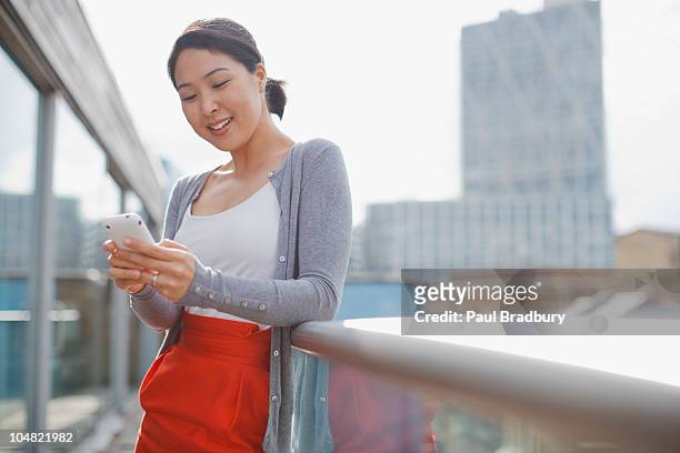 smiling businesswoman text messaging with cell phone on urban balcony - mobile phone reading low angle stock pictures, royalty-free photos & images