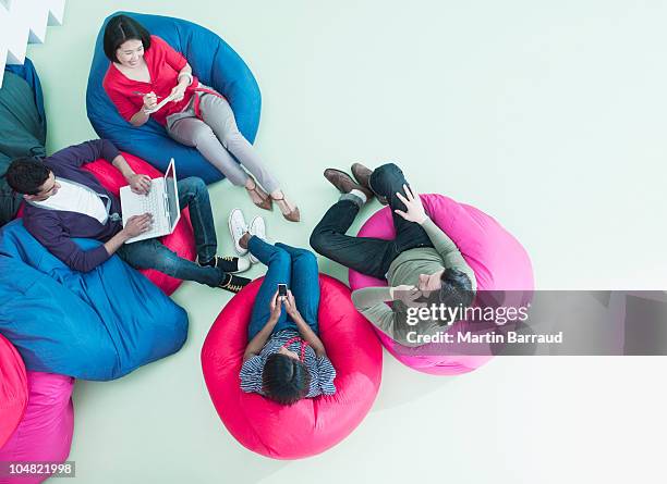 men and women using laptop and cell phones in bean bag chairs - sitting chair office relax stockfoto's en -beelden