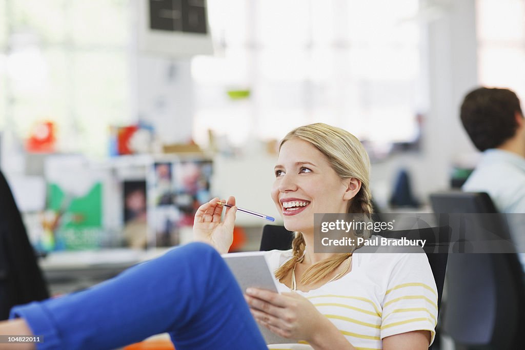 Smiling businesswoman holding notepad and looking up in office