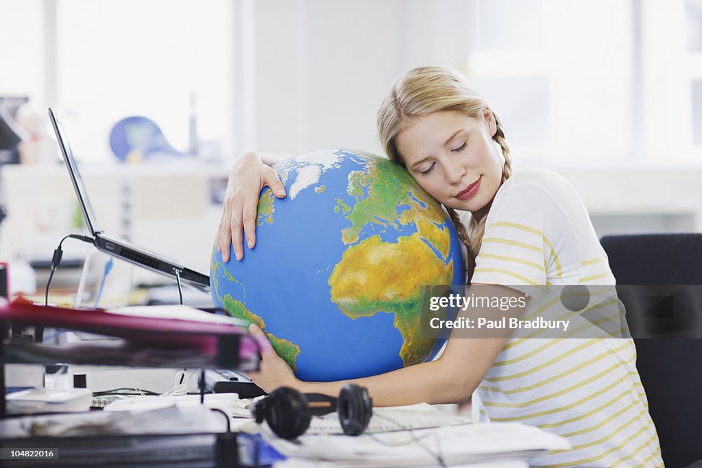 Businesswoman with eyes closed hugging globe at desk in office