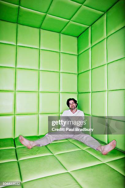 hombre sentado con piernas separadas en habitación acolchada - camisa de fuerza fotografías e imágenes de stock