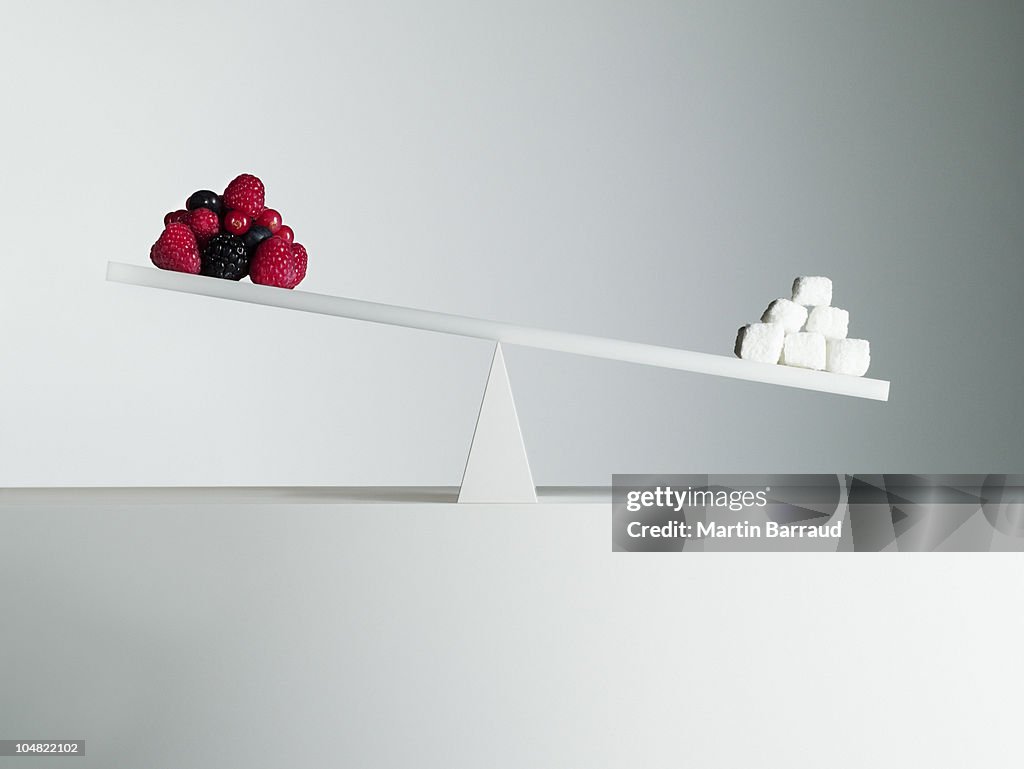 Sugar cubes tipping seesaw with berries on opposite end