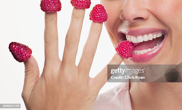 close up of woman biting raspberries on fingertips - no face stockfoto's en -beelden