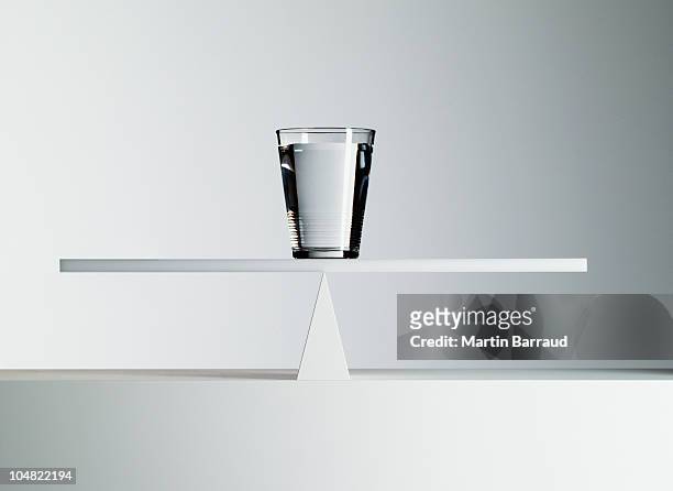 glass of water balancing on middle of seesaw - scales balance 個照片及圖片檔