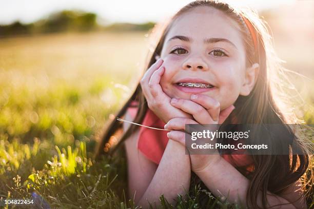 young girl in grass smiling - braces 個照片及圖片檔