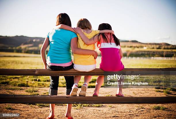 3 young girls sitting on fence - alleen meisjes stockfoto's en -beelden