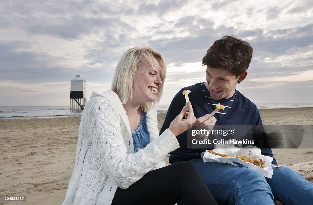 Couple on beach eating fish and chips