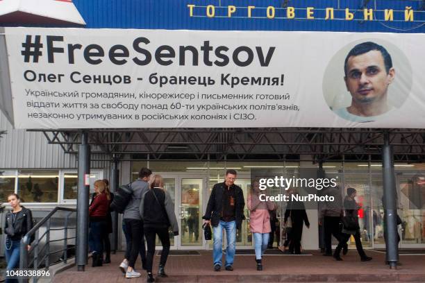 People walk past a poster with a photo of Ukrainian film director Oleg Sentsov and with the hashtag &quot;FreesSentsov&quot;, displayed at the...