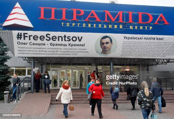 People walk past a poster with a photo of Ukrainian film director Oleg Sentsov and with the hashtag &quot;FreesSentsov&quot;, displayed at the...