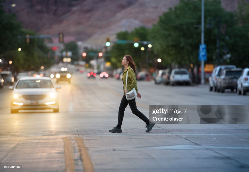 Woman in american small city traffic crossing road, mountains in background