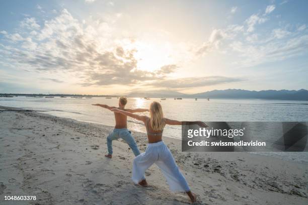 healthy young couple exercising yoga outdoors on the beach at sunrise in a tropical climate, bali, indonesia. people healthy balance concept - sunrise yoga stock pictures, royalty-free photos & images