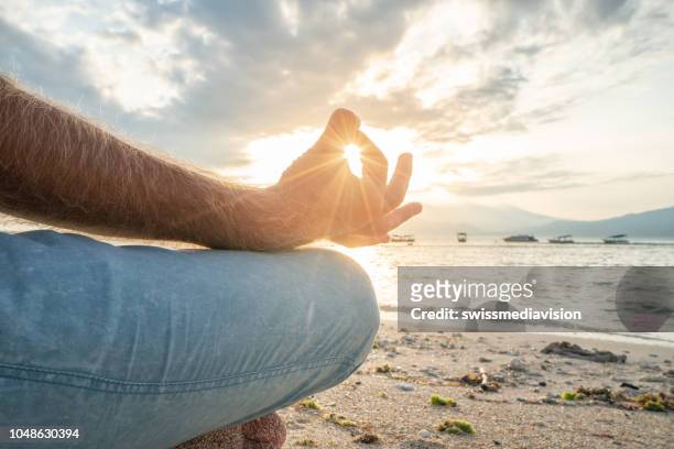 hautnah am mann, hält yoga lotussitz meditieren am strand bei sonnenaufgang in einem tropischen klima, bali, indonesien. menschen gesunde balance konzept - body men close up stock-fotos und bilder