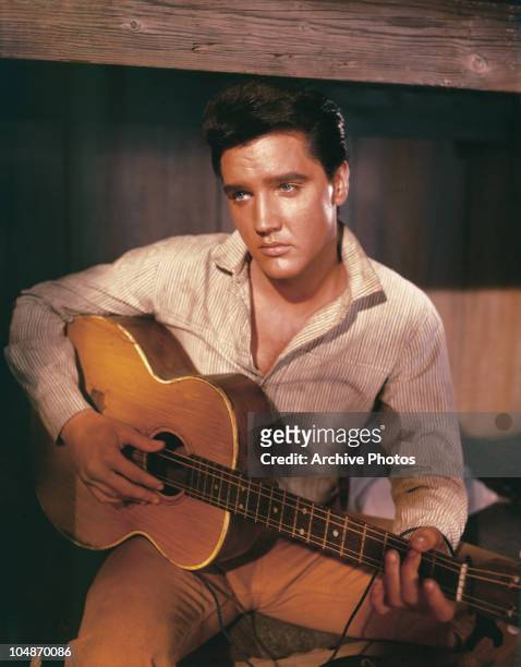 Portrait of American singer and actor Elvis Presley holding an acoustic guitar circa 1956.