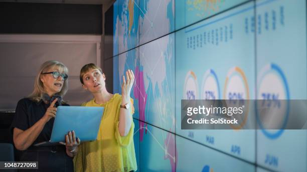 businesswomen discussing ideas against an information wall - people infographic imagens e fotografias de stock