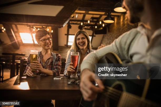 zwei glückliche frauen spaß in einer bar, während der mann akustische gitarre spielt. - music pub stock-fotos und bilder