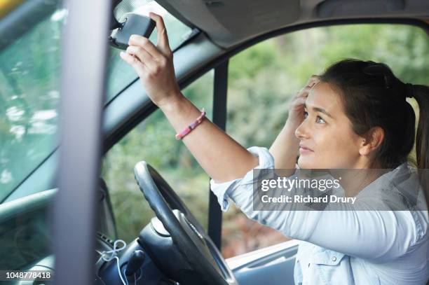 young woman using the rear mirror of her van to adjust her hair - adjusting hair stock pictures, royalty-free photos & images