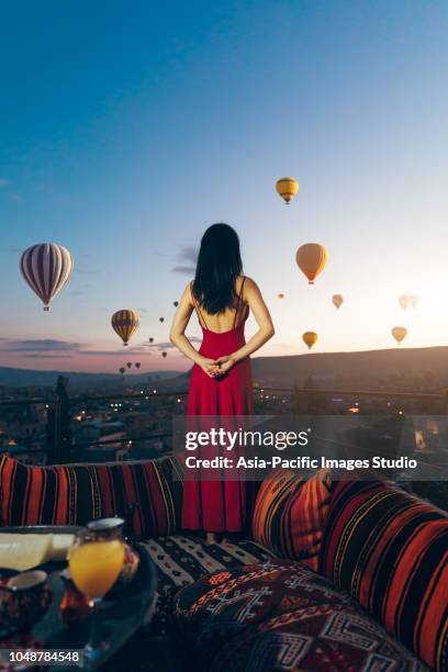back view of beautiful asian woman watching colorful hot air balloons flying over the valley at cappadocia, turkey.turkey cappadocia fairytale scenery of mountains. turkey cappadocia fairytale scenery of mountains. - capadócia imagens e fotografias de stock