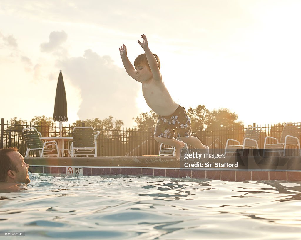 Young boy jumping off edge of pool