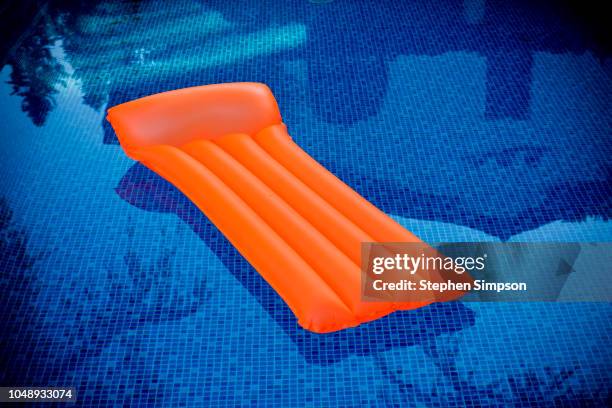 orange plastic raft floats in blue tiled swimming pool - pool raft stock pictures, royalty-free photos & images