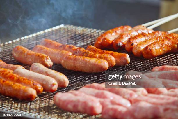 sausages on grill grate being grilled on the street at event - carne procesada fotografías e imágenes de stock