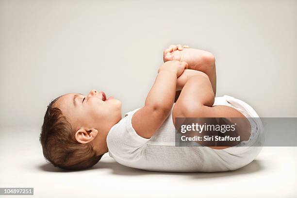 baby laying on back holding feet smiling - baby studio stock-fotos und bilder