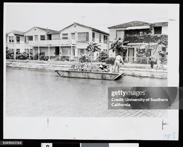 Photograph of a city employee cleaning one of the canals in Venice, CA 'Neat homes line one of few well-kept sections of canal. City employee on...