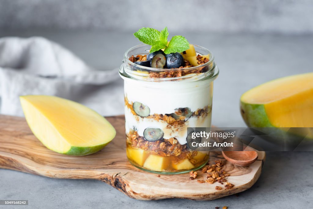 Breakfast yogurt parfait with granola, mango, berries in jar