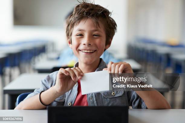 boy laughing and holding paper note, sitting in classroom - boy brown hair stock pictures, royalty-free photos & images