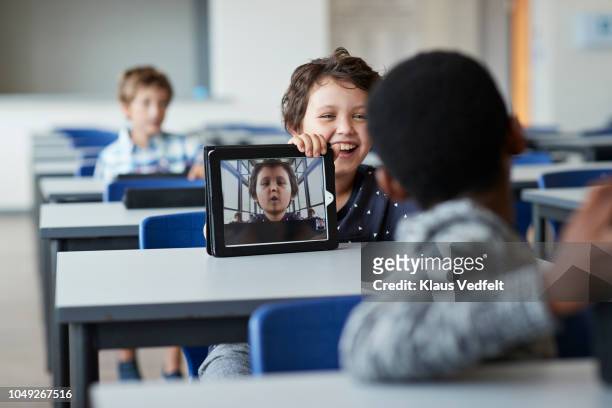 laughing boy showing funny selfie to class mate - school tablet stock-fotos und bilder