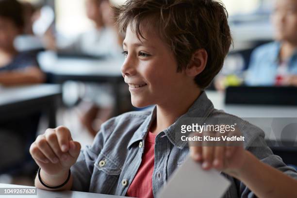 Boy laughing and holding paper note, sitting in classroom