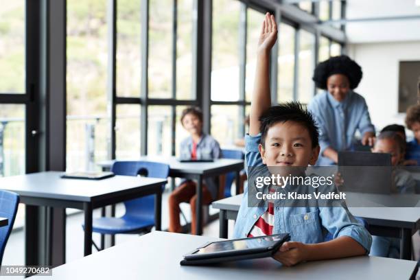 schoolboy with raised hand in classroom - kids modern school life stock-fotos und bilder