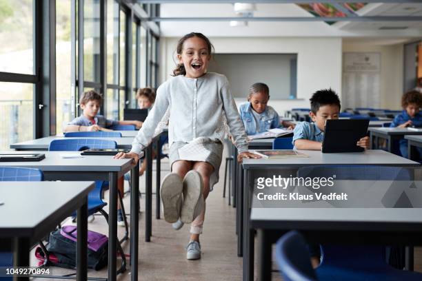 happy girl balancing between tables with feet in the air in classroom - classroom play stockfoto's en -beelden