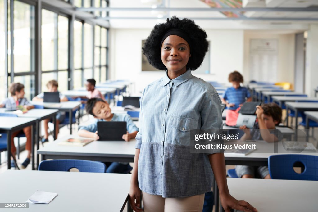 Portrait of female teacher standing in classroom with students in background