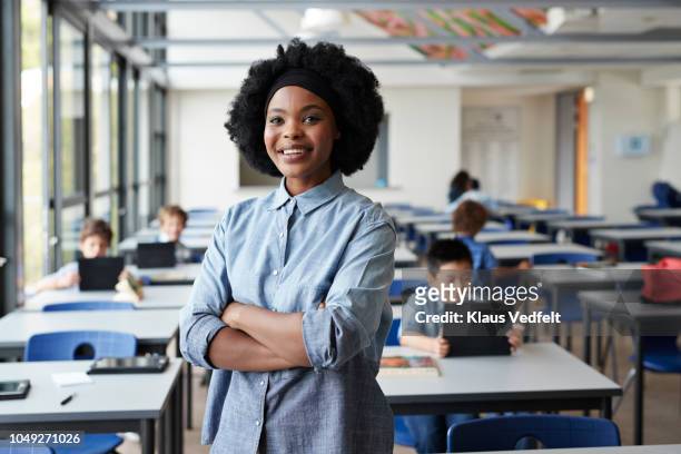 portrait of female teacher standing in classroom with students in background - school pride stock pictures, royalty-free photos & images