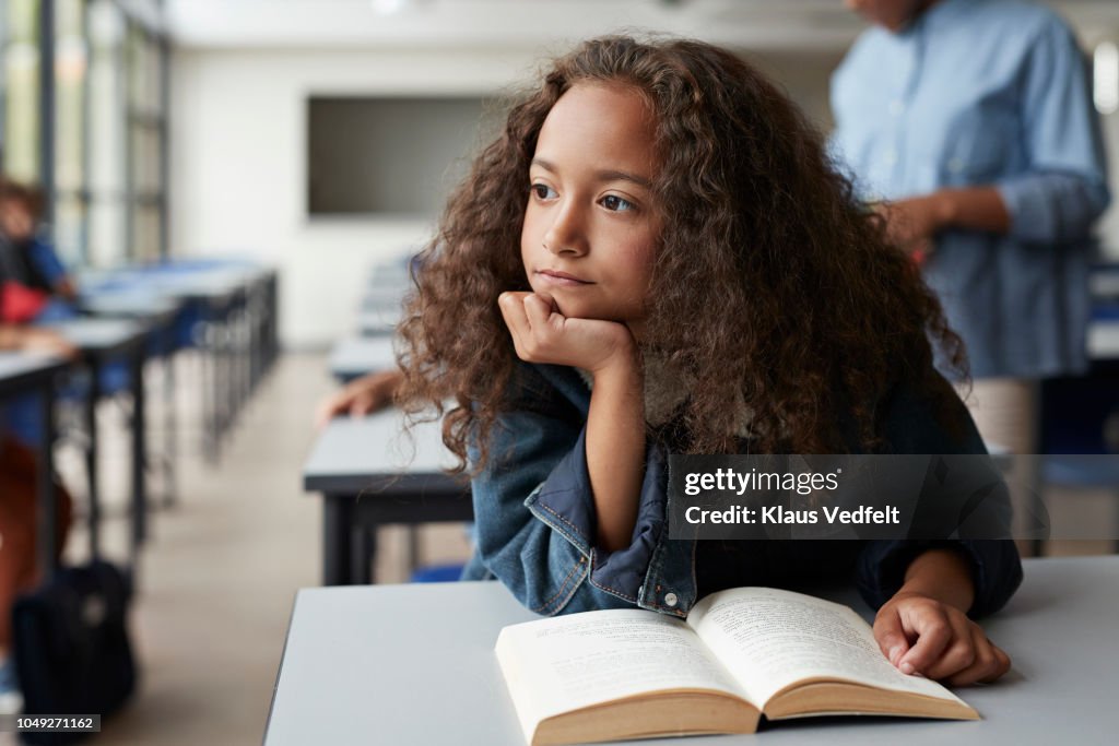 Girl sitting with book and looking thoughtful out of window