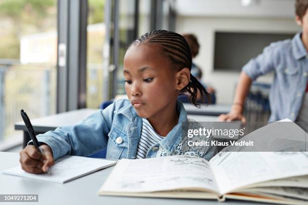 girl writing in book in classroom - african cornrow braids stock pictures, royalty-free photos & images