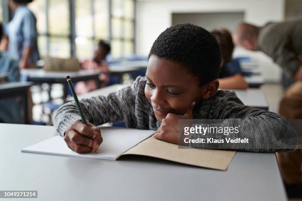 boy writing in book in classroom - schoolboy stock pictures, royalty-free photos & images