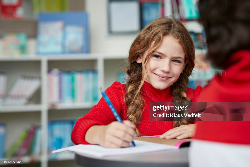 Portrait of cute schoolgirl drawing at the library