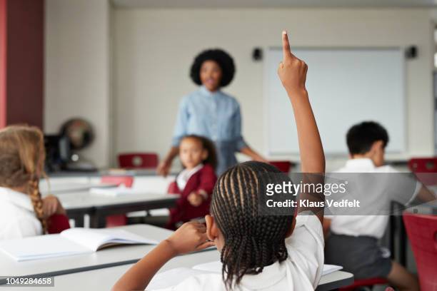 Focus on schoolgirls raised hand in classroom with teacher