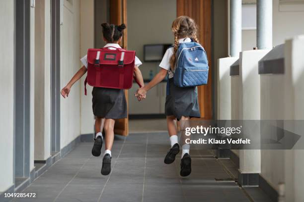 schoolgirls running hand in hand on the isle of school and laughing - rugzak stockfoto's en -beelden
