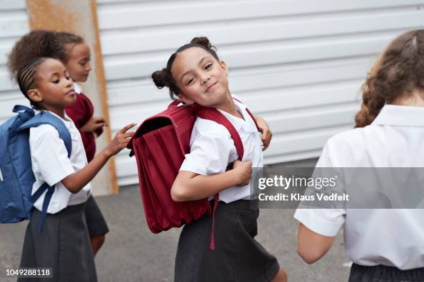 cute schoolgirl looking to camera while walking from school with friends - uniforme scolastica foto e immagini stock