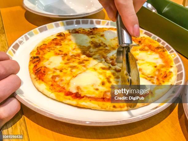 man’s hands cutting pizza with pizza cutter at italian food restaurant in yokohama at lunchtime - ピザカッター ストックフォトと画像