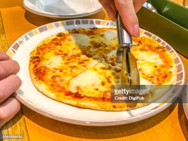 man’s hands cutting pizza with pizza cutter at italian food restaurant in yokohama at lunchtime - pizzaskärare bildbanksfoton och bilder