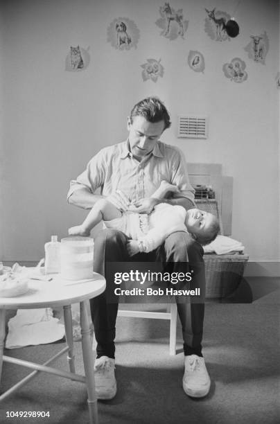 Sussex and England cricketer Ted Dexter pictured changing the nappy of his baby son Tommy in a nursery at home in England on 19th April 1963.