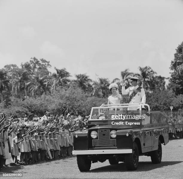 Queen Elizabeth II and Prince Philip, Duke of Edinburgh pictured waving to crowds of cheering school children from the rear of an open top Land Rover...